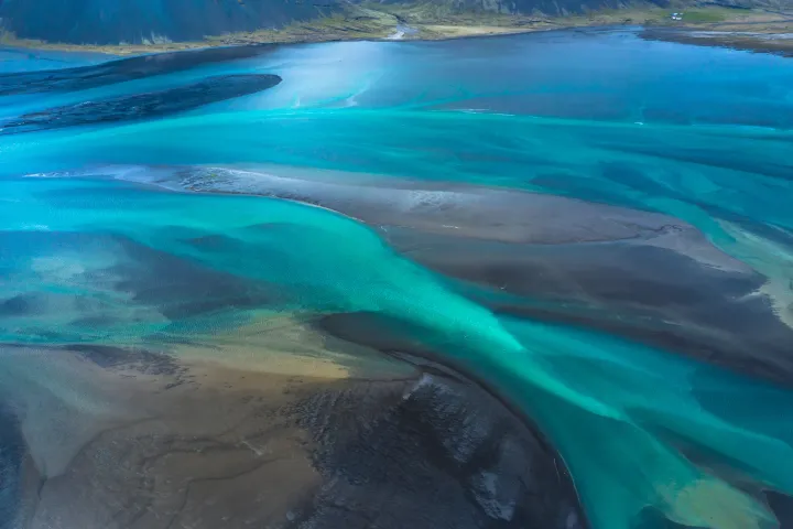 Aerial view of a braided turquoise river delta over black sand