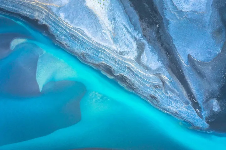 Aerial abstract of turquoise water meeting textured rock